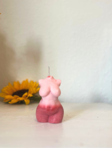 Pink candle shaped like a torso on a white surface with a blurred background