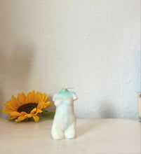 Load image into Gallery viewer, Small white with blue and green female torso candle figurine with a sunflower on a light surface against a plain background
